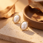 Pearl earrings with gold frames on a beige surface with leaves